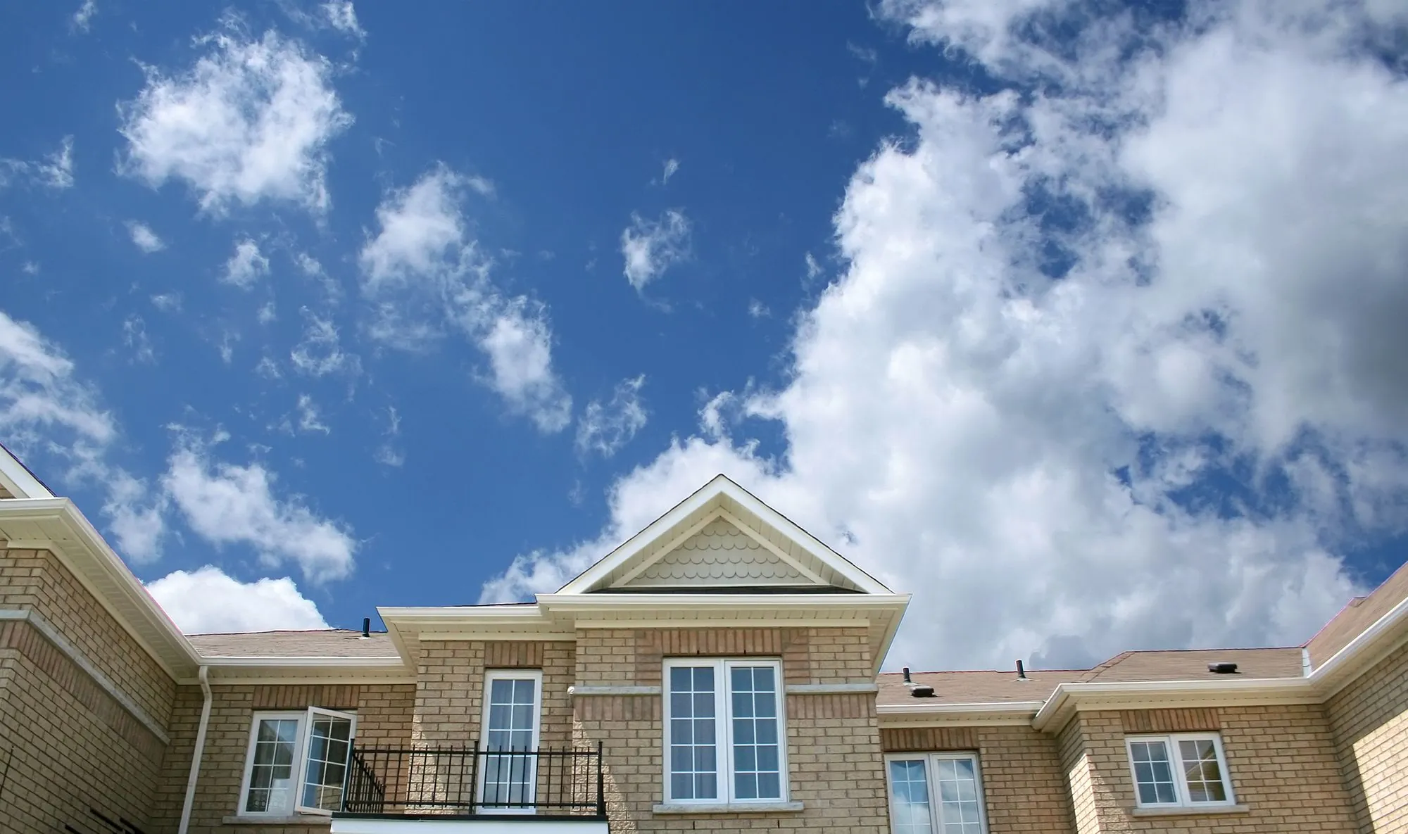 A brick house with steep gables under a bright, cloudy sky